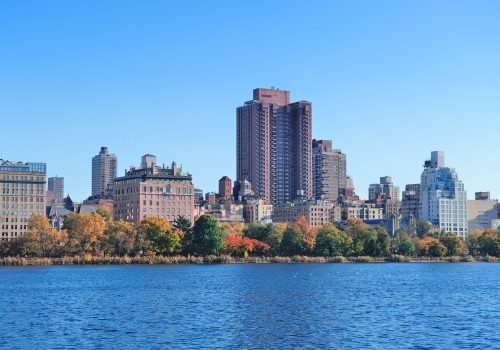 Central Park Autumn with New York City Manhattan Midtown skyline skyscrapers over lake with colorful foliage and clear blue sky.