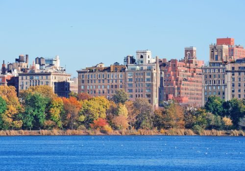 Central Park Autumn with New York City Manhattan Midtown skyline skyscrapers over lake with colorful foliage and clear blue sky.